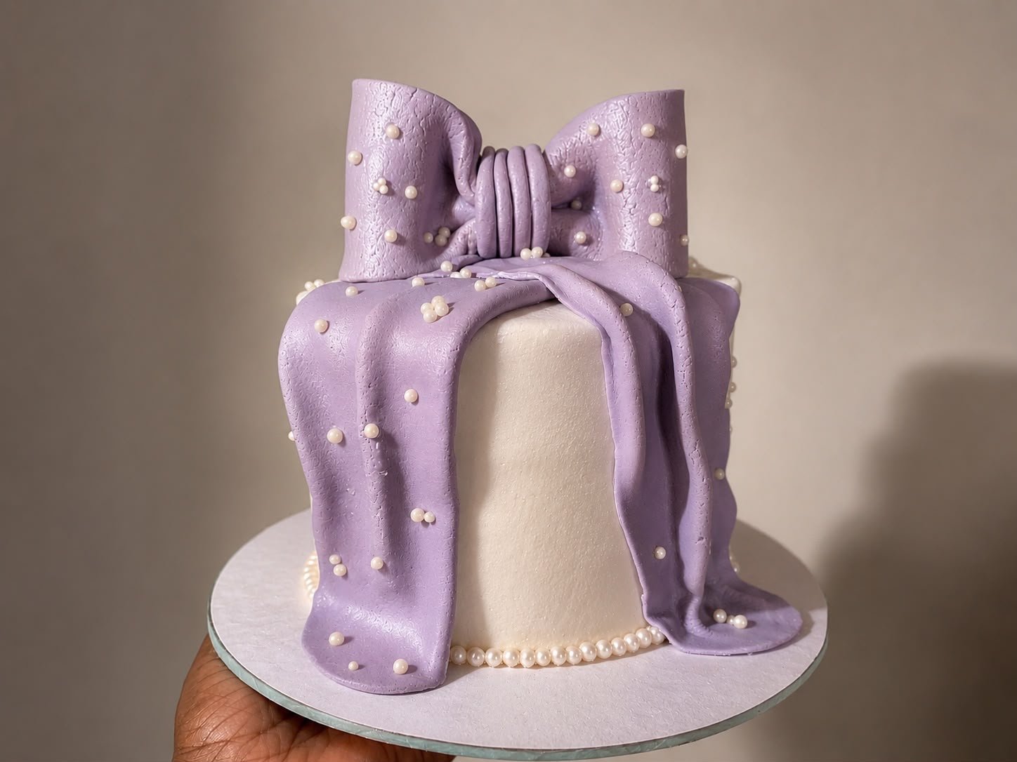 Elegant ivory celebration cake wrapped in a lilac fondant bow with pearls